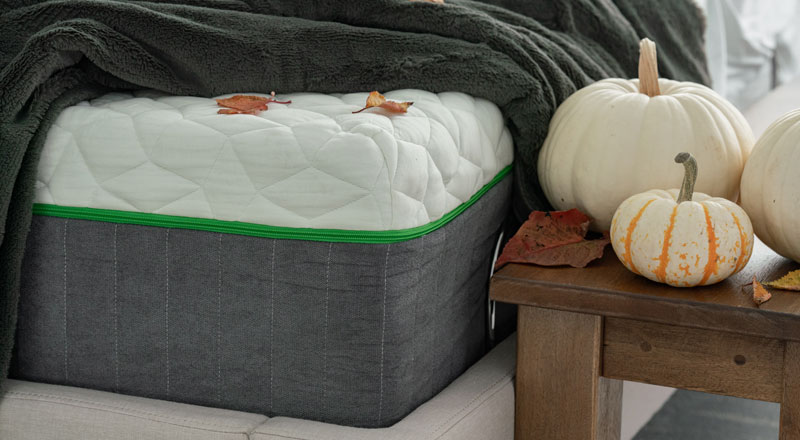 mattress with a blanket on top and fall pumpkins to the side